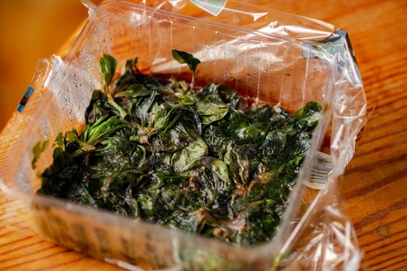 Plastic food container filled with spoiled spinach.