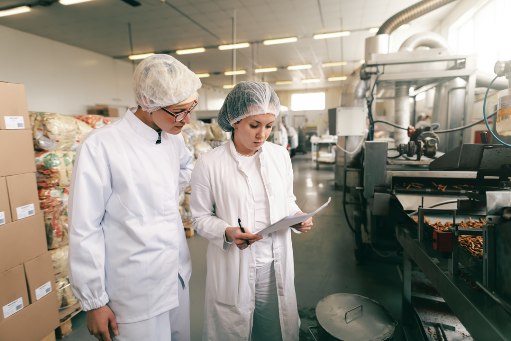 Two people in white uniforms on food production line evaluating safety and quality. 