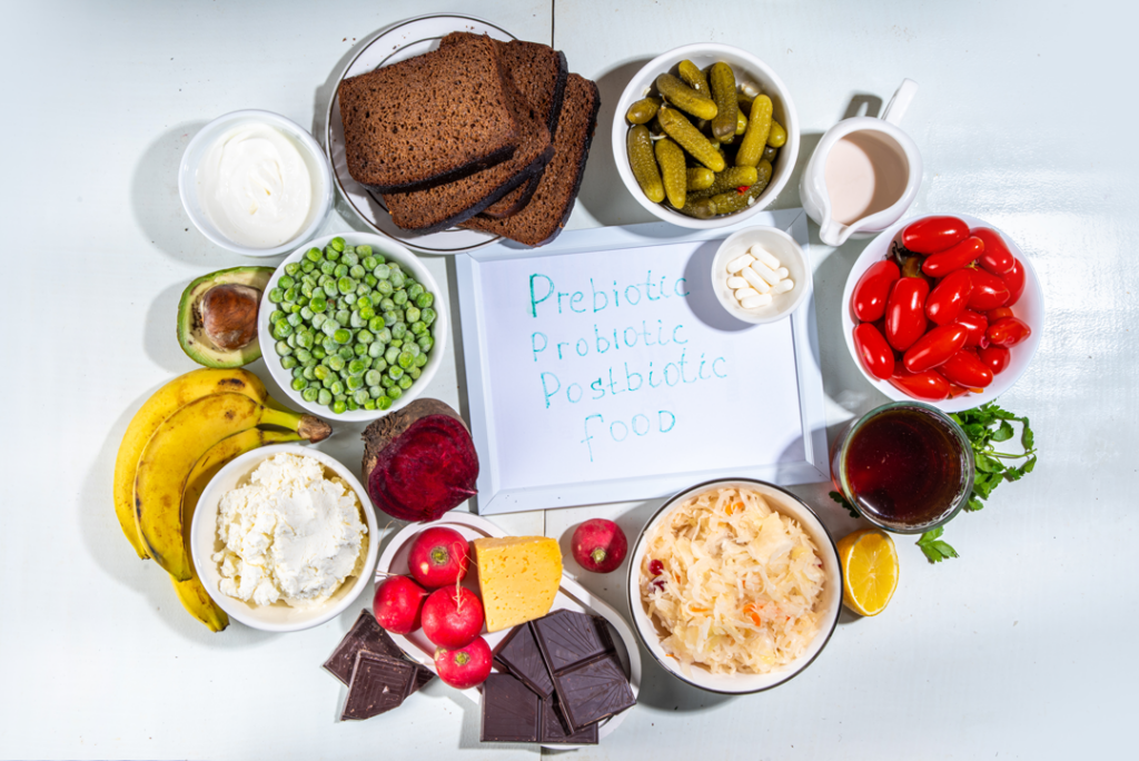 Bowls of food surrounding a white board on which is written prebiotic, probiotic, and postbiotic.  