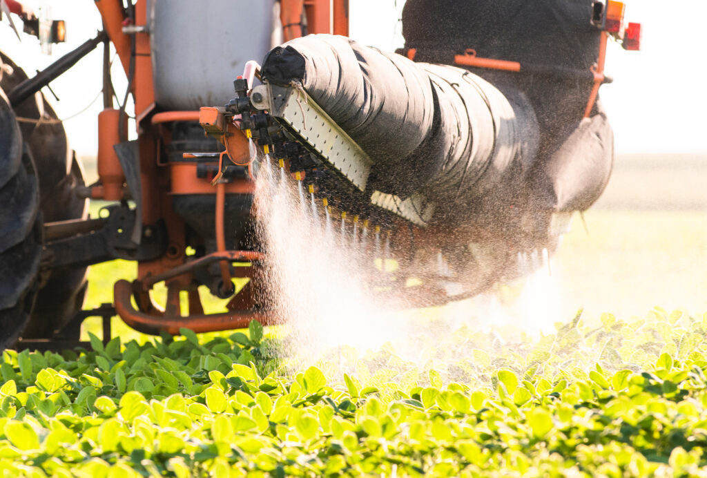 Tractor spraying pesticide onto plants growing in field. 