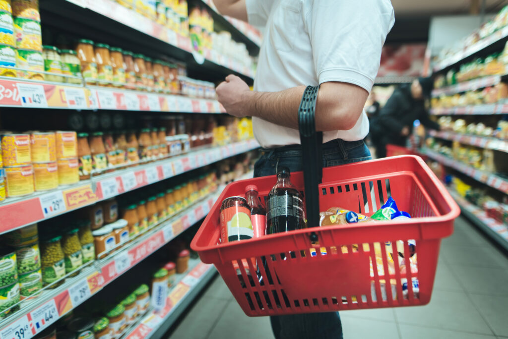 Man standing in grocery store with basket of food looking at items on the shelf.