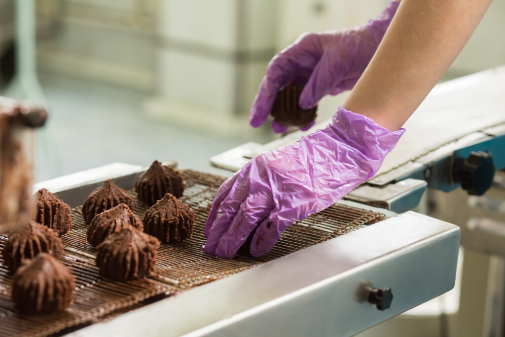 Person wearing purple latex gloves placing chocolate on production line in a processing plant.