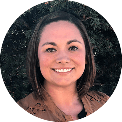 Smiling woman portrait outdoors with evergreen branches in the background.